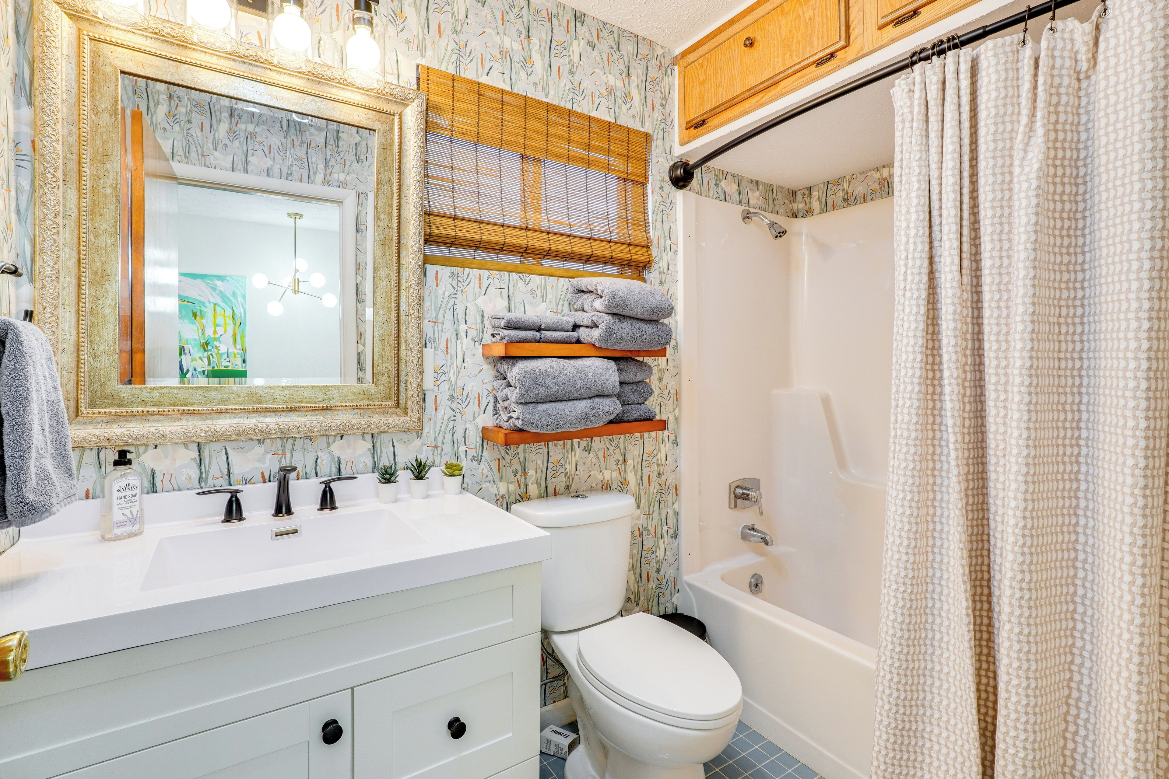 A bathroom with a white sink, a toilet, and a bathtub. There is a shelf with towels and a mirror above the sink.