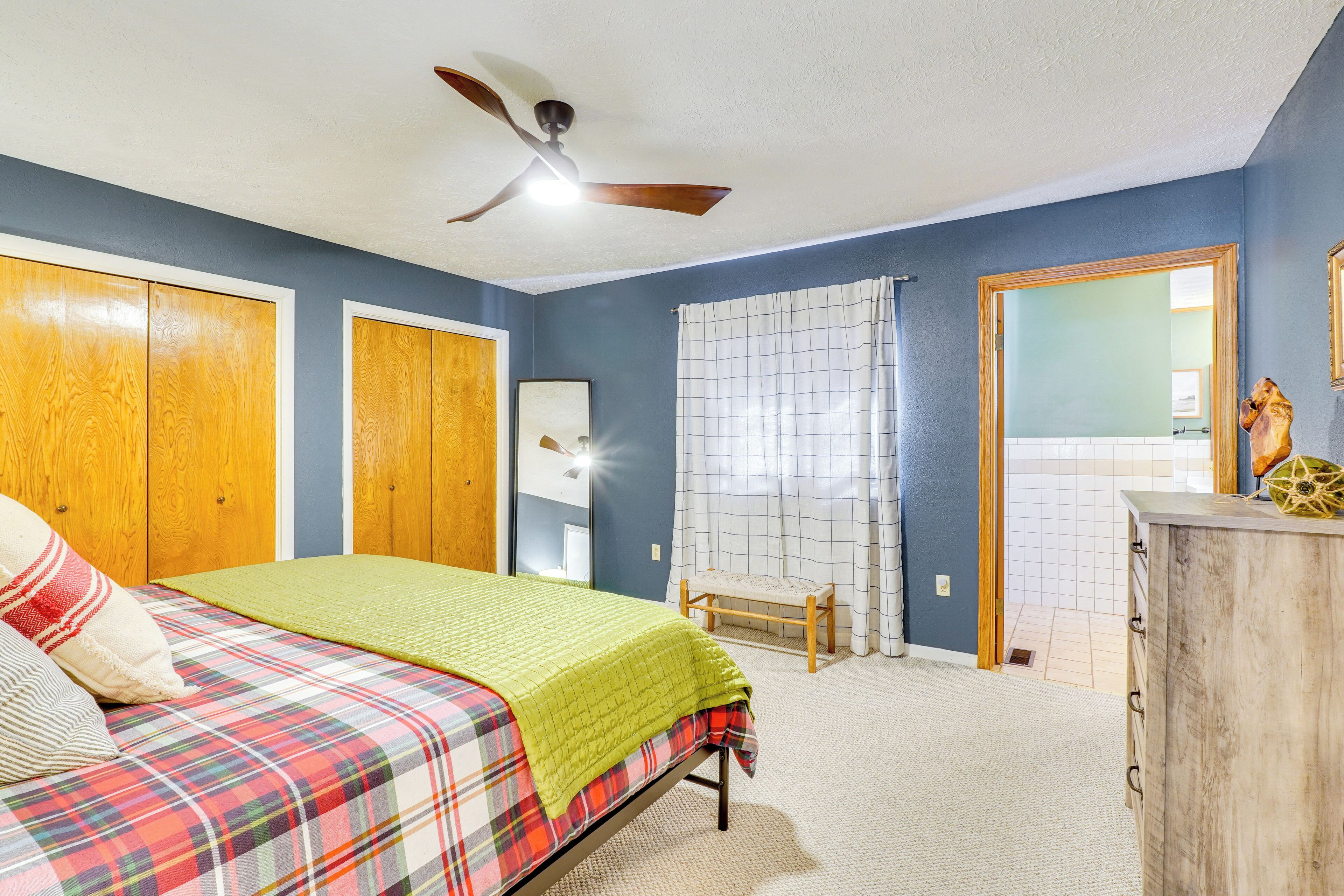 Un dormitorio con una cama, un ventilador de techo, un armario de madera y una ventana con cortinas.