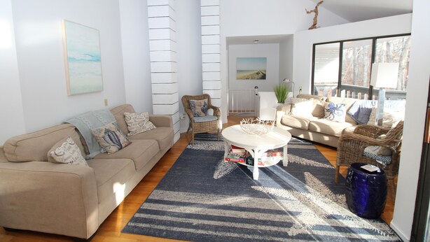 Un salón amplio con un sofá color beige, una mesa de centro blanca y una alfombra azul estampada.