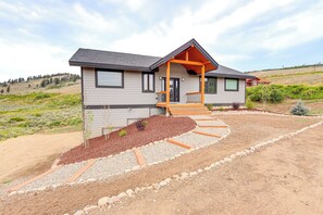 A modern single-story house with a covered porch, a landscaped front yard with gravel and mulch, and a hilly landscape in the background.