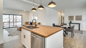 Een moderne keuken met een centraal kookeiland, een roestvrijstalen vaatwasser, hangende lampen en een eethoek met een tafel en stoelen.