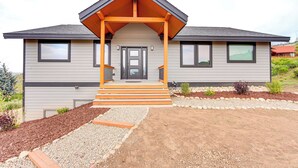 Een modern huis met twee verdiepingen, een overdekte veranda, een voordeur en een kleine tuin met mulch en grind.
