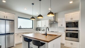 Een moderne keuken met witte kasten, een centraal eiland met krukken, roestvrijstalen apparatuur en hanglampen.