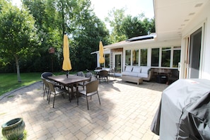 Eine Terrasse im Freien mit Esstisch und Stühlen, gelben Sonnenschirmen und einem überdachten Sitzbereich.