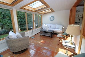 A sunlit room with a sofa, a wicker chair, a coffee table, and a lamp. - Spacious Home With Private Yard Close to Beach Abutting Conservation (2397) (Brewster)