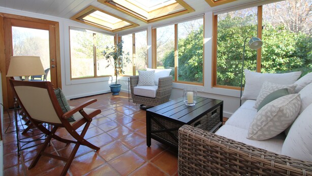 Une pièce lumineuse, baignée de soleil, avec un canapé, des fauteuils et une table, dotée de grandes fenêtres et d’une lucarne.