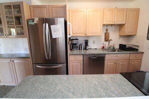 A kitchen with a stainless steel refrigerator, wooden cabinets, a granite countertop, and a dishwasher. - Spacious Home With Private Yard Close to Beach Abutting Conservation (2397) (Brewster)