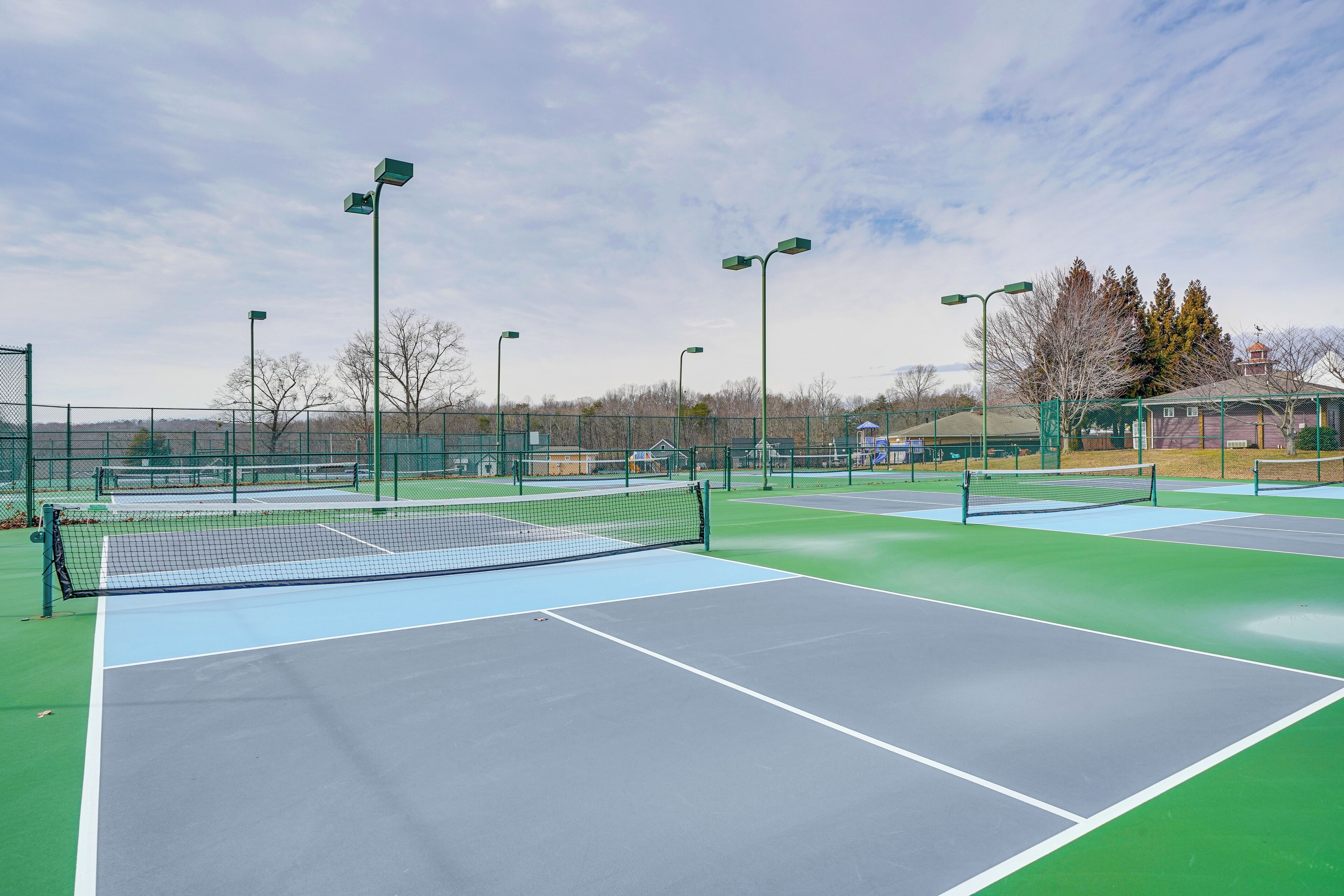 A tennis court with multiple courts, green and blue surfaces, and surrounding fencing.