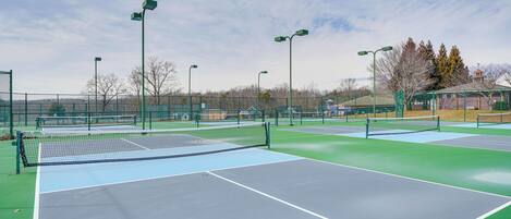 A tennis court with multiple courts, green and blue surfaces, and surrounding fencing.