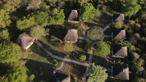 An aerial view of a rural property with thatched-roof cottages arranged in a circular pattern around a central courtyard, connected by stone pathways. - savannah murchison lodge (Paraa)