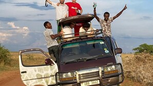 A vehicle with passengers on the roof, a clear sky, and a dirt road. - savannah murchison lodge (Paraa)