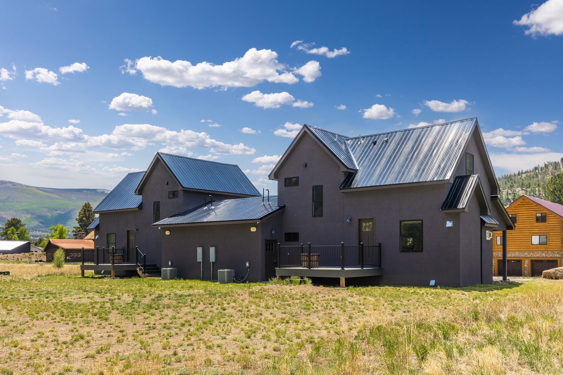 Une maison moderne à deux étages, dotée d’un toit en métal, de grandes fenêtres et d’une extension à toit plat.
