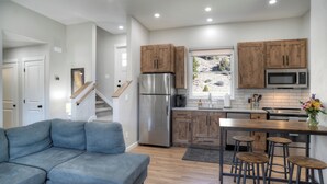 A modern kitchen with wooden cabinets, stainless steel appliances, and a bar area with stools. - Newly Built Duplex | A/C | Peekaboo River Views | Cozy Interior (South Fork)