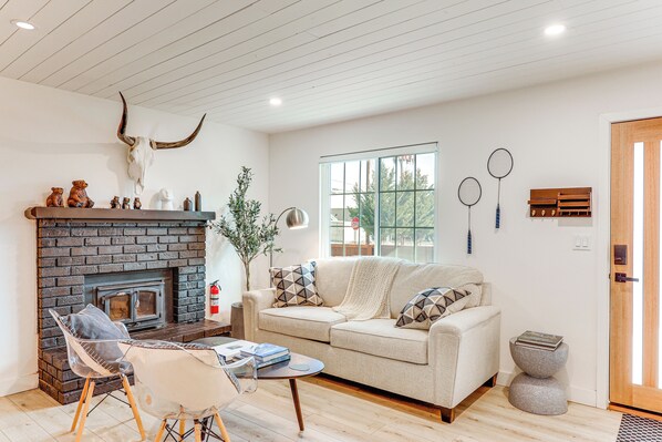 A living room with a fireplace, a sofa, a coffee table, and a chair. - Fish, Hike & Explore: Cabin w/ Yard in Big Bear (Big Bear City)
