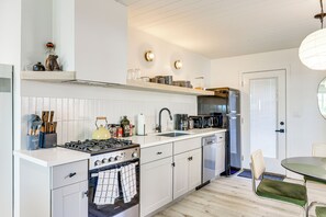 A modern kitchen with white cabinetry, a stove, sink, and a dining area with a table and chairs. - Fish, Hike & Explore: Cabin w/ Yard in Big Bear (Big Bear City)