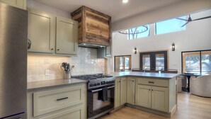 A modern kitchen with light green cabinets, a stainless steel refrigerator, and a large island with a built-in stove.