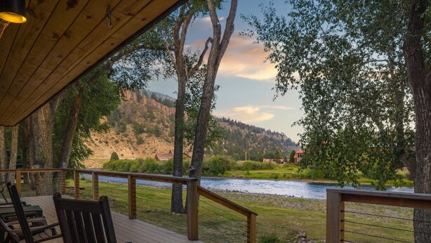 A wooden deck with chairs overlooking a river and hills.