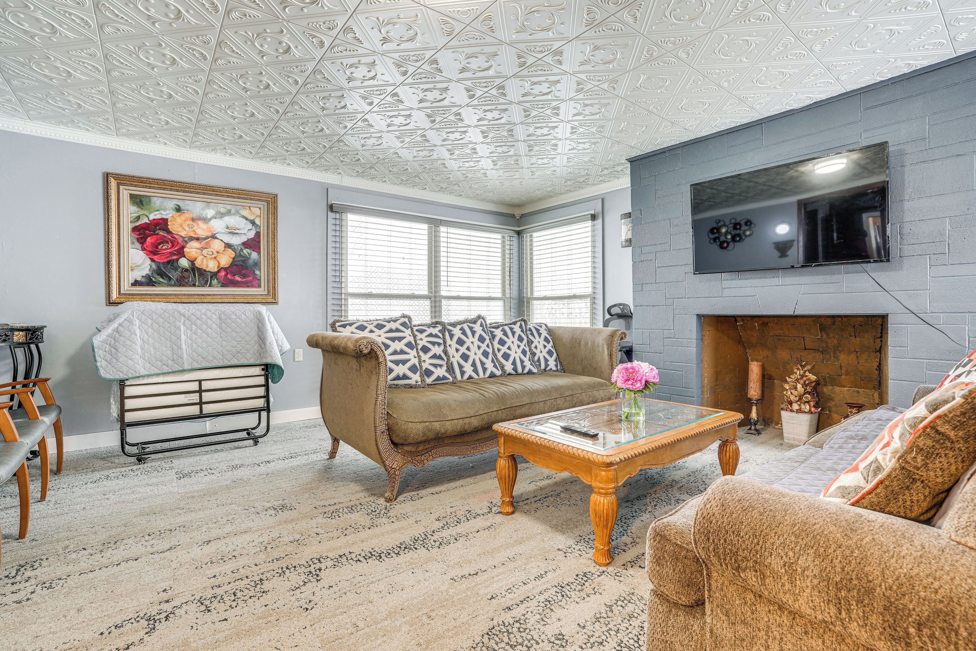 Un salon avec un plafond orné de motifs, une cheminée, un canapé, une table basse et un tableau accroché au mur.