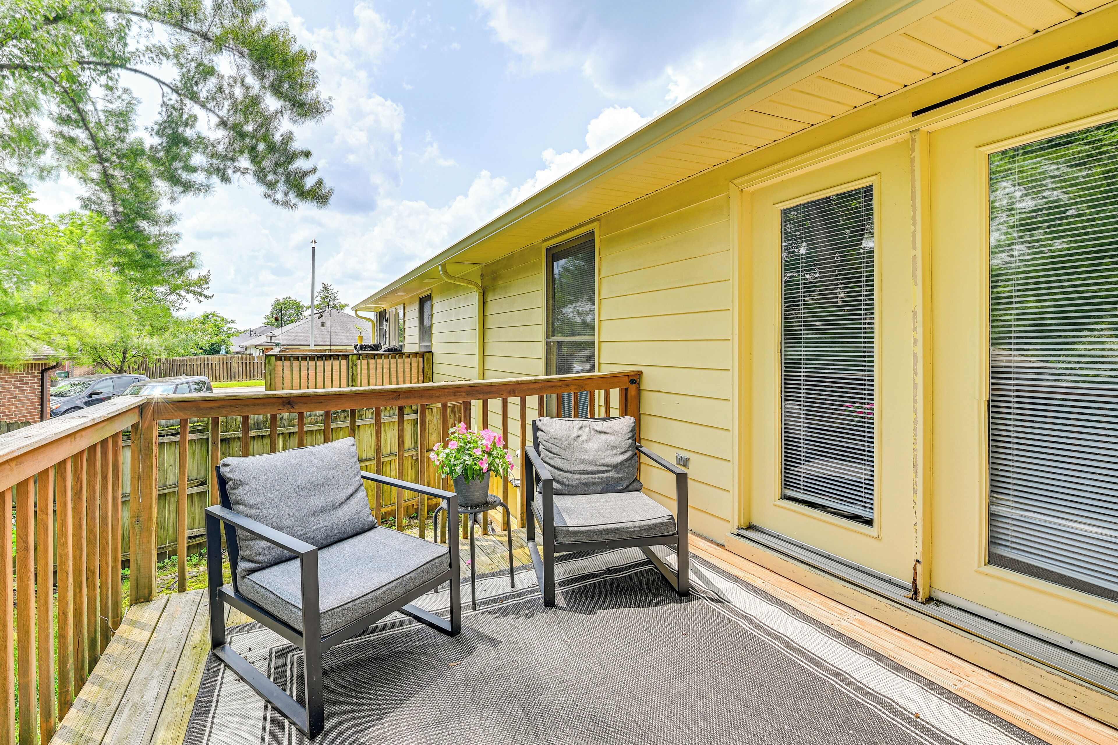 A deck with two chairs and a small table, a wooden railing, and a yellow building with large windows.