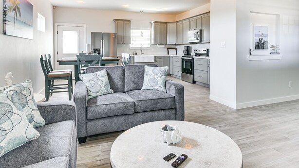 A modern living room with a grey sofa, a round coffee table, and a kitchen in the background. - Modern Port Isabel Home: Coastal Family Home! (Port Isabel)