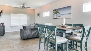 A dining area with a wooden table and teal chairs, a gray sofa, and a ceiling fan. - Modern Port Isabel Home: Coastal Family Home! (Port Isabel)