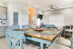 A dining area with a wooden table, light blue chairs, and a ceiling fan. - Modern Port Isabel Home: Coastal Family Home! (Port Isabel)