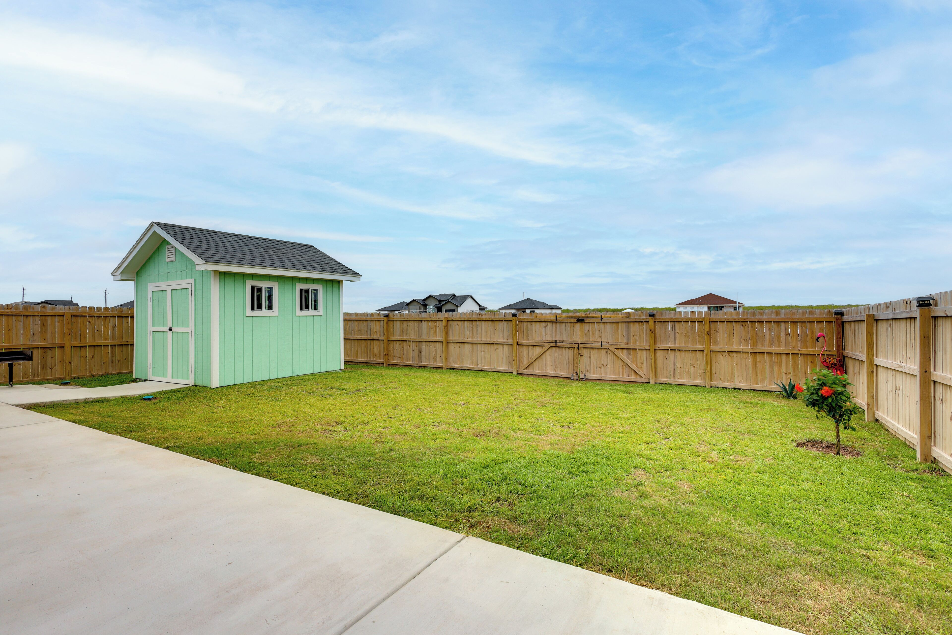 Un jardin avec un abri de jardin vert, une clôture en bois et un petit arbre.