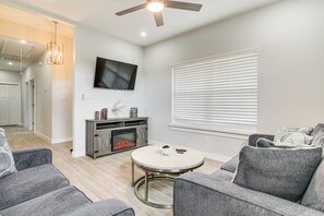 A modern living room with a fireplace, grey sofas, a round coffee table, and a ceiling fan. - Modern Port Isabel Home: Coastal Family Home! (Port Isabel)