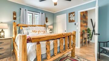 A bedroom with a wooden bed, a ceiling fan, a nightstand, a lamp, and a window with curtains.