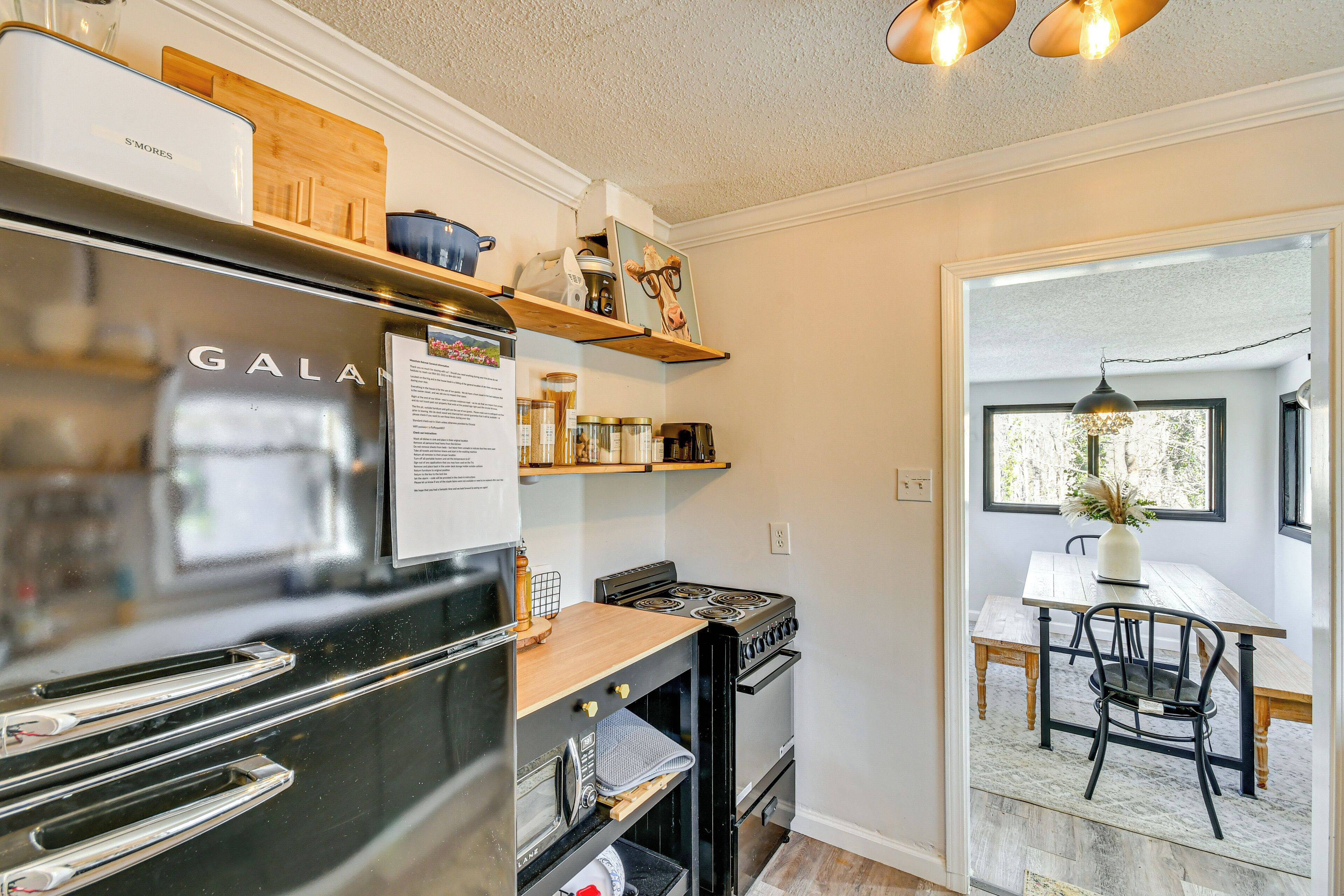 A compact kitchen with a refrigerator, stove, oven, and wooden shelves.