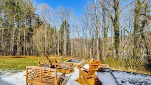 Eine Holzterrasse mit Gartenmöbeln, einer Feuerstelle und einem verschneiten Wald im Hintergrund.