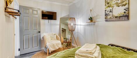 A room with a bed, a chair, a mirror, and a painting on the wall.
