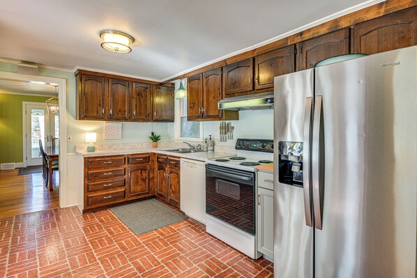 A kitchen with wooden cabinets, a stainless steel refrigerator, a dishwasher, and a brick-patterned floor. - Waterfront Reedville Retreat w/ Hot Tub + Dock (Reedville)