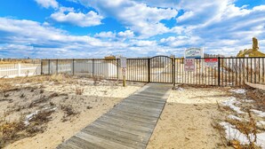 Una entrada a la playa con un pasillo de madera que conduce a la arena, una cerca blanca y un cartel de la Asociación de Playas Elizabeth Carter.