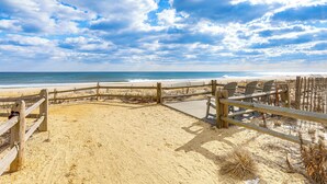 Un paseo marítimo de madera que conduce a una playa arenosa con una valla de madera y sillas.