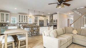 Una cocina amplia con electrodomésticos modernos, un comedor con mesa y sillas de madera, y una sala de estar con sofá color crema.
