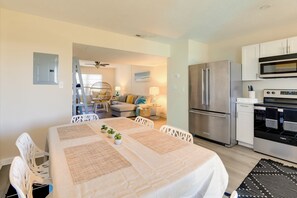 A modern kitchen with stainless steel appliances, a dining area with a table set for four, and a living area with a sofa and a lamp. - 1/2 Mi to Atlantic Beach: Townhome w/ Balcony! (Atlantic Beach)
