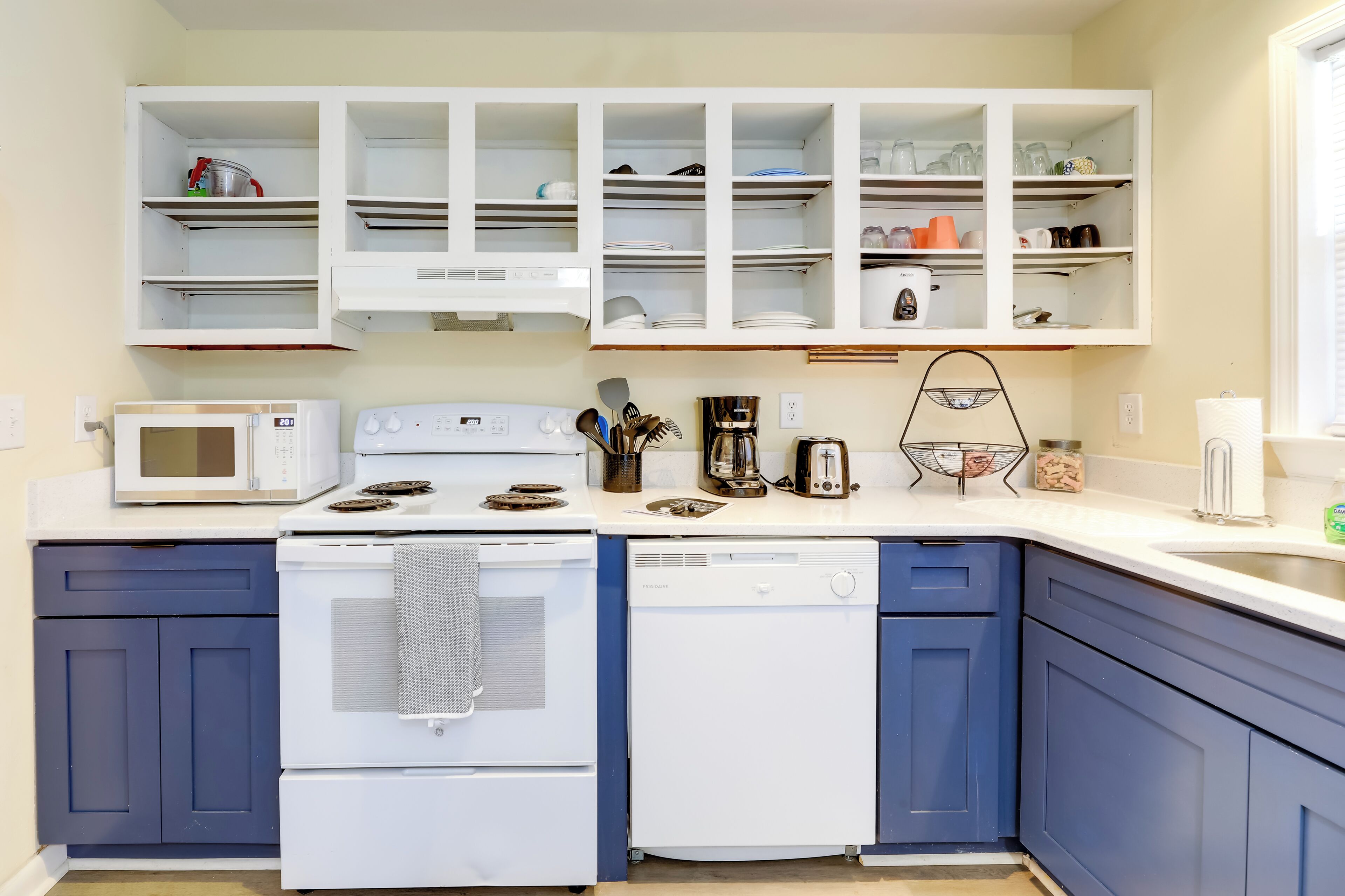 A kitchen with white appliances, blue cabinets, and white upper cabinets.