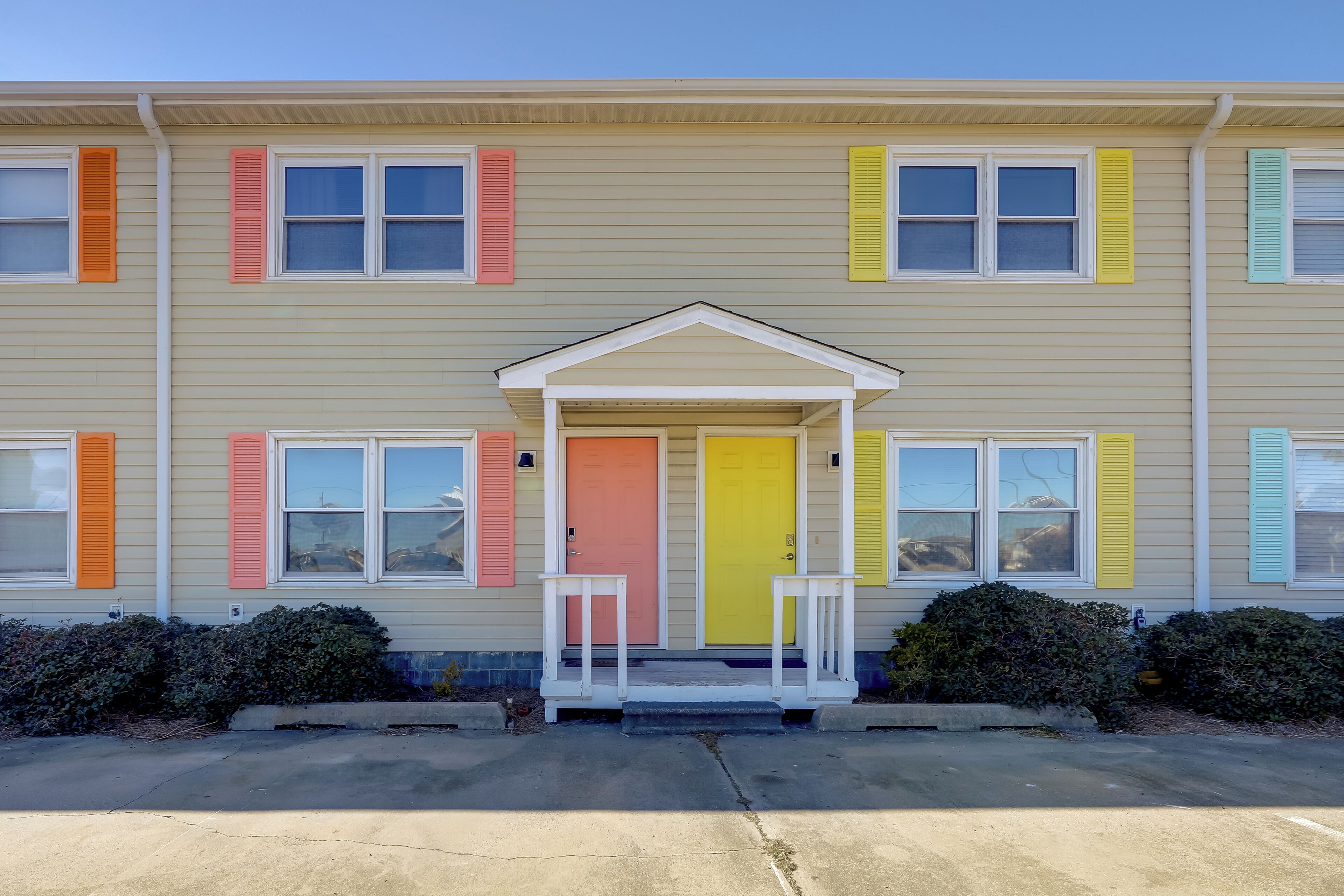 A multi-story building with a beige exterior, a central entrance with a white porch, and colorful shutters on the windows.