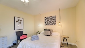 A bedroom with a bed, a chair, a small table, and a wall-mounted lamp. - Walk to Atlantic Beach: Townhome w/ Patio! (Atlantic Beach)