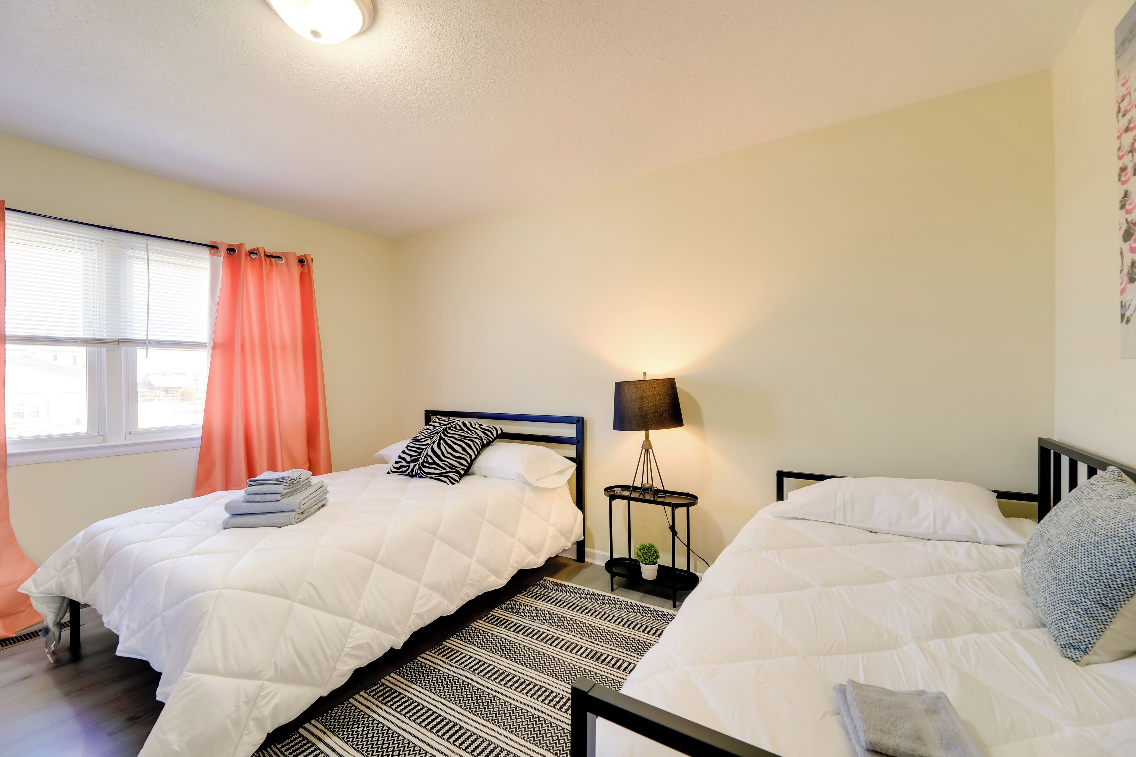 A bedroom with two beds, a nightstand with a lamp, and a window with curtains.