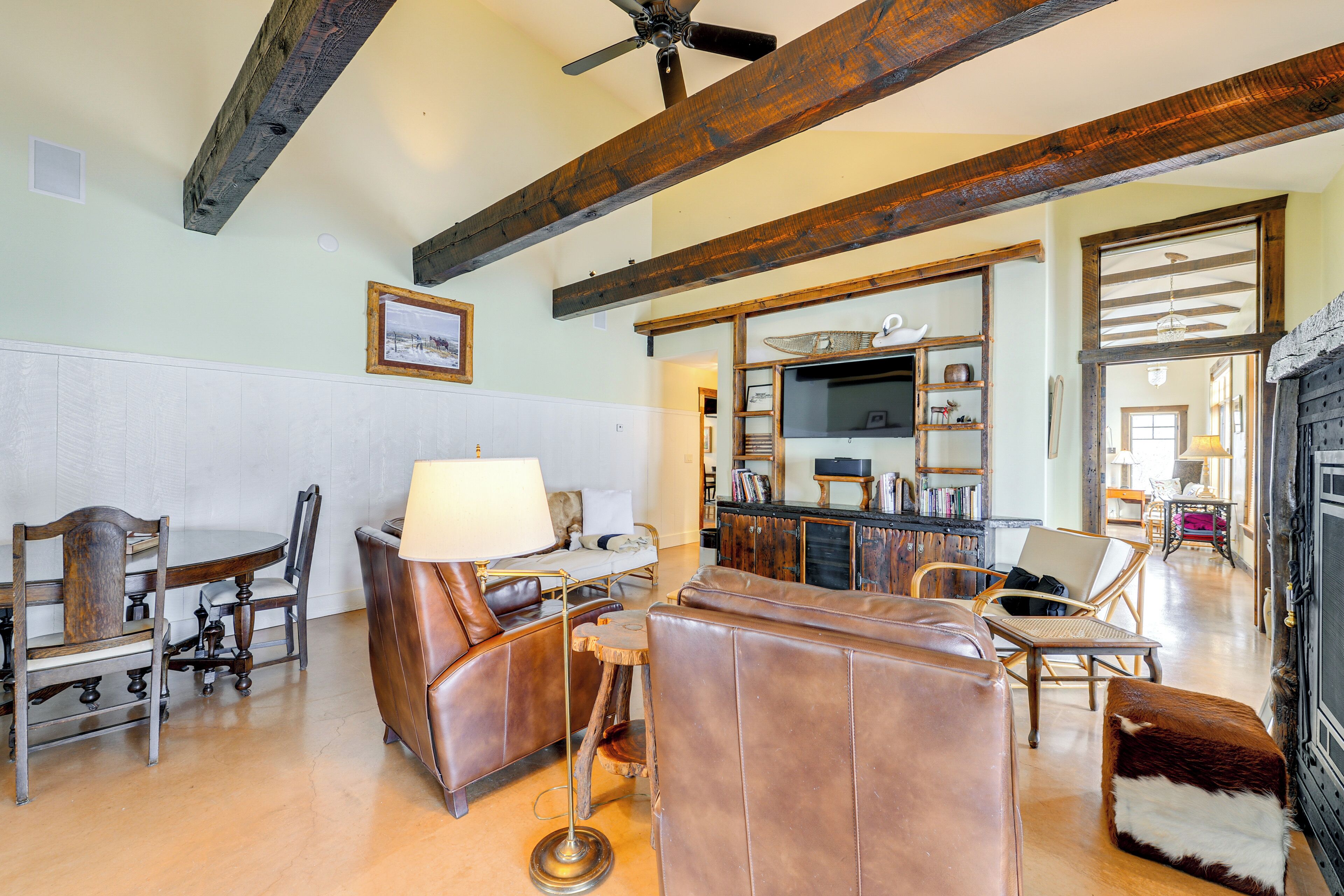 A spacious living room with wooden beams, leather sofas, a dining table, and a fireplace.