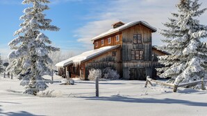 A rustic wooden cabin with a snow-covered roof, surrounded by snow-laden trees.