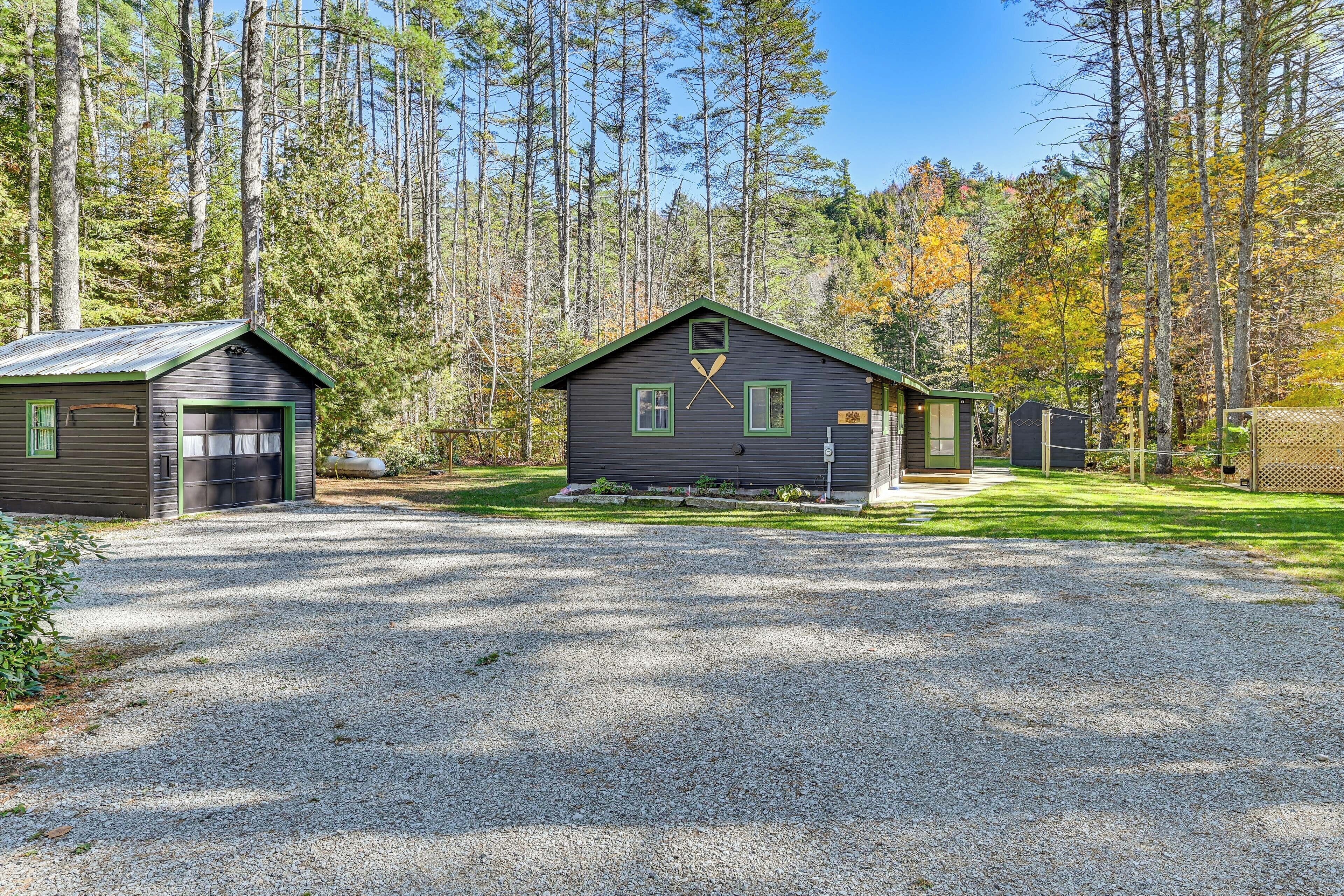 A cabin with a gravel driveway, surrounded by tall trees and a clear sky.