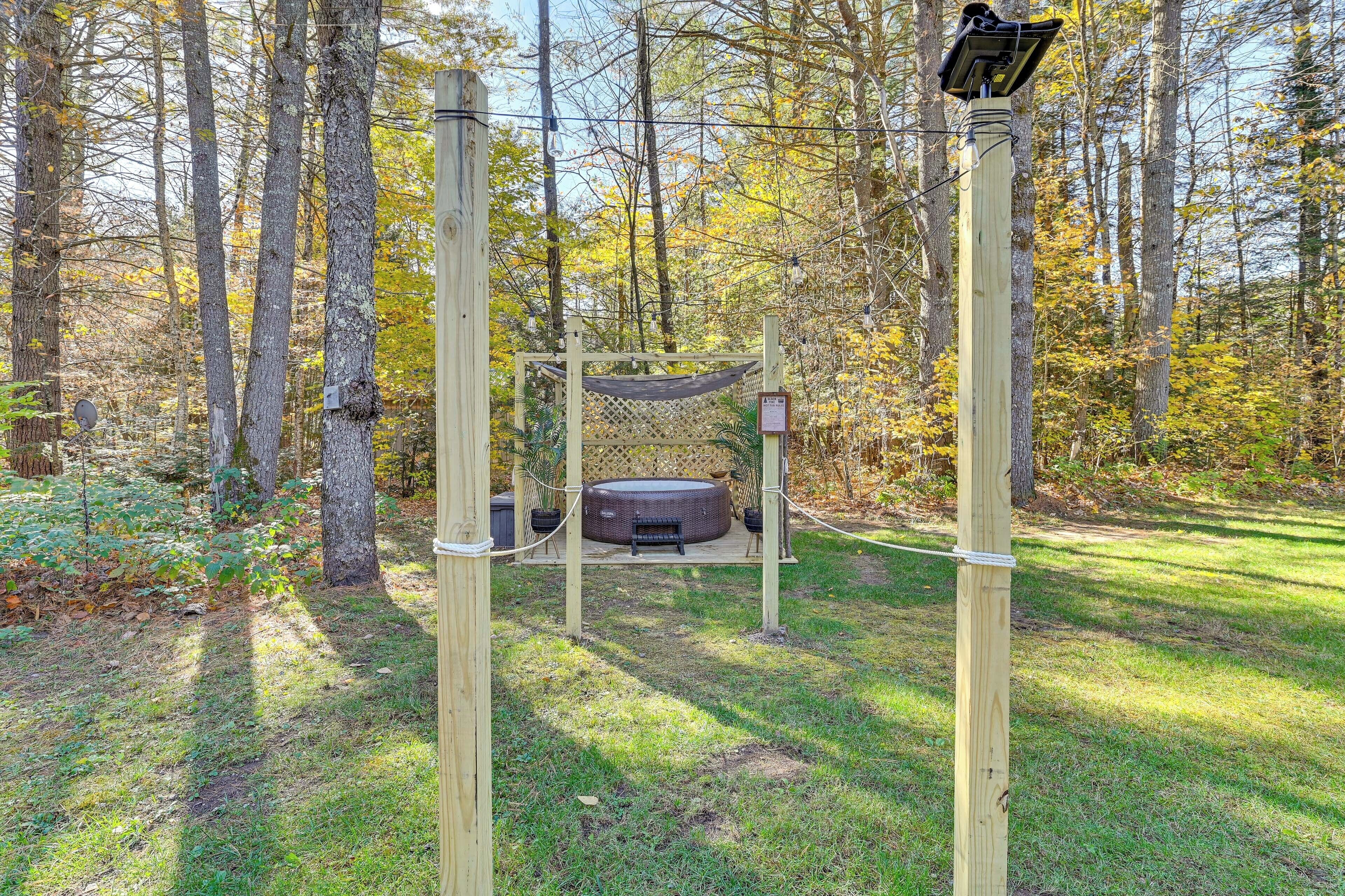 A hammock suspended between two wooden posts in a wooded area with a hot tub below.