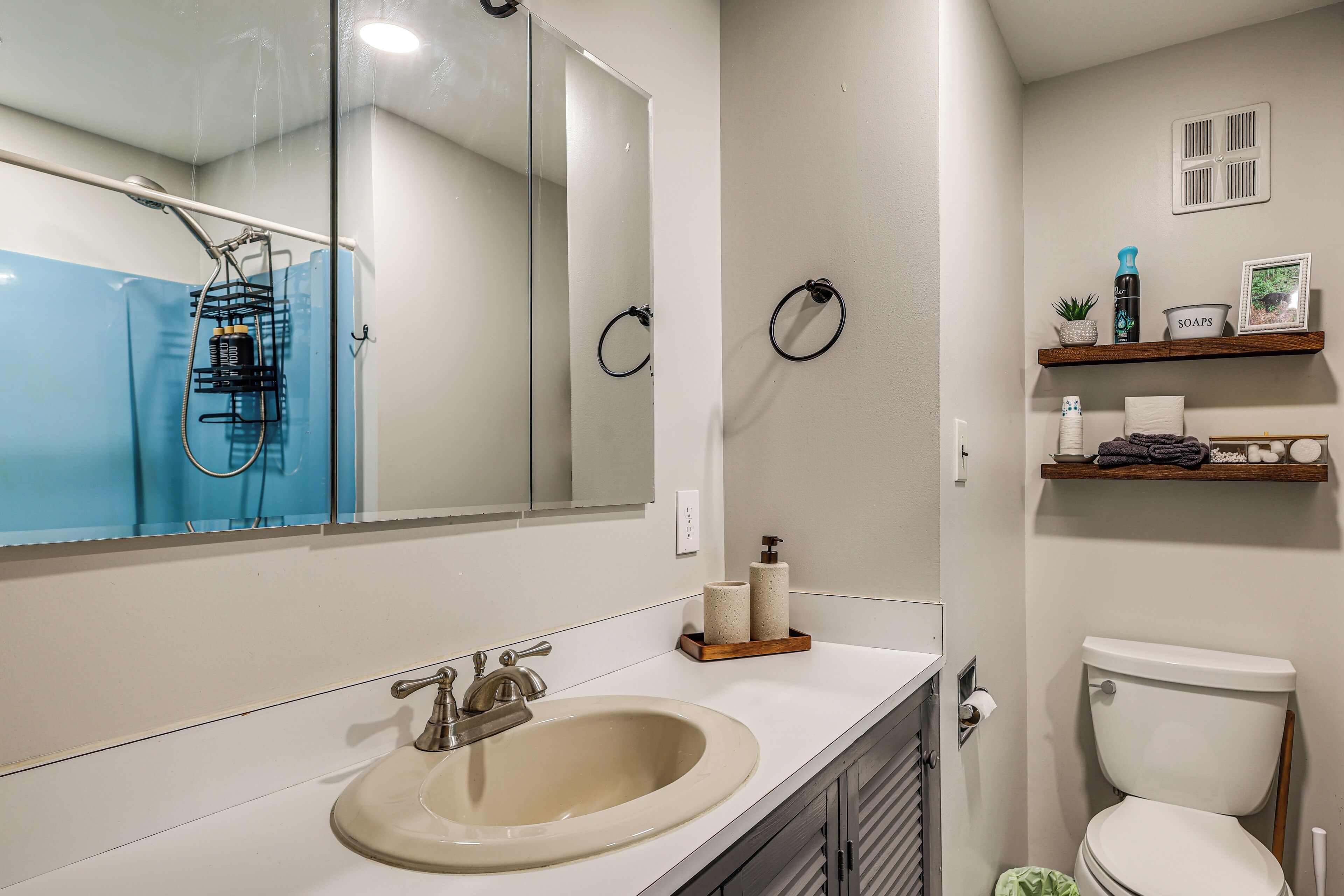 Een badkamer met een wastafel, spiegel, toilet en planken met toiletartikelen.
