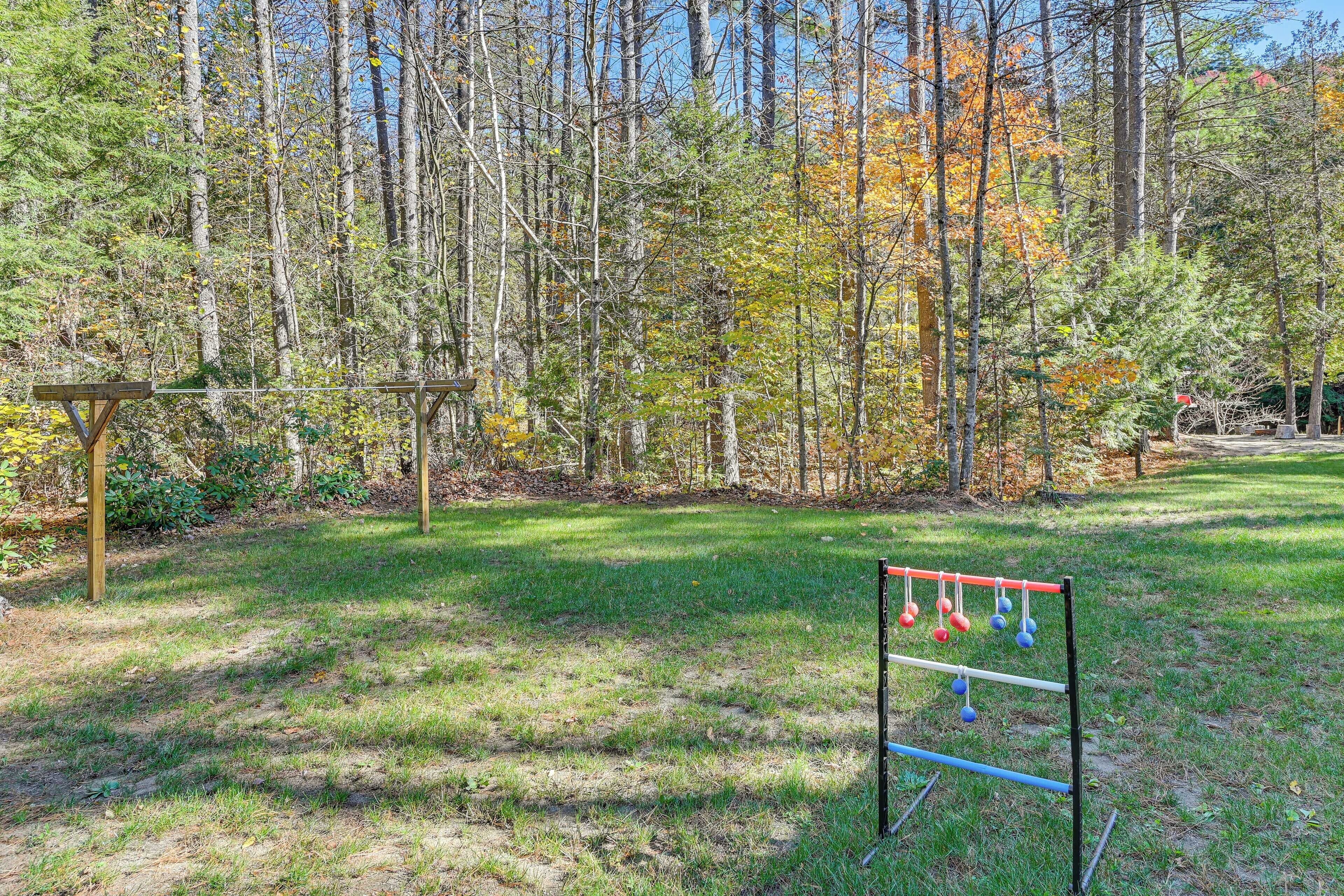 A grassy area with a metal structure holding colorful balls, surrounded by trees with autumn foliage.