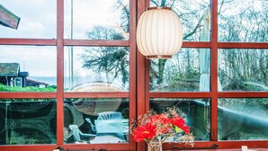 Ett rum med stora fönster, en hängande lampa och en vas med röda blommor på ett bord.