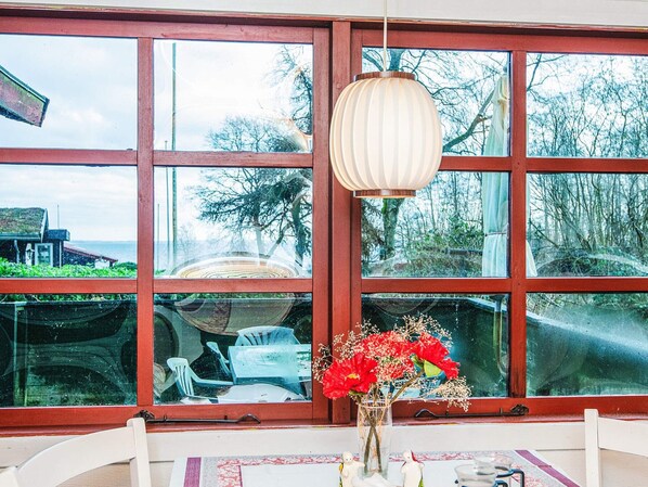 Ein Zimmer mit großen Fenstern, einer hängenden Leuchte und einer Tischvase mit roten Blumen.