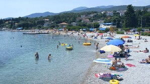 A beach with clear water, people swimming, and colorful umbrellas. - Luxury apartment in Opatija for 8 people with pool and silk bedding (Opatija)